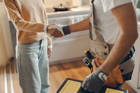Customer shaking hands with a technician wearing a tool belt, symbolizing service completion or agreement.